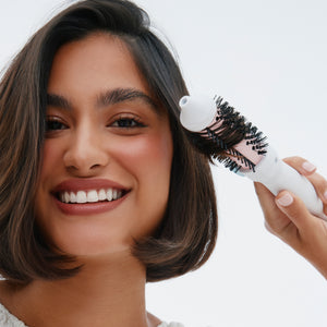 Woman using a hairbrush on her hair with a plain background