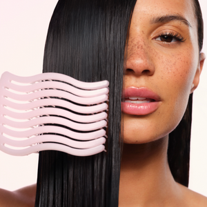 A close-up of a woman with straight, dark hair holding a light pink wavy hair comb against her hair, showing how the comb glides through the strands.