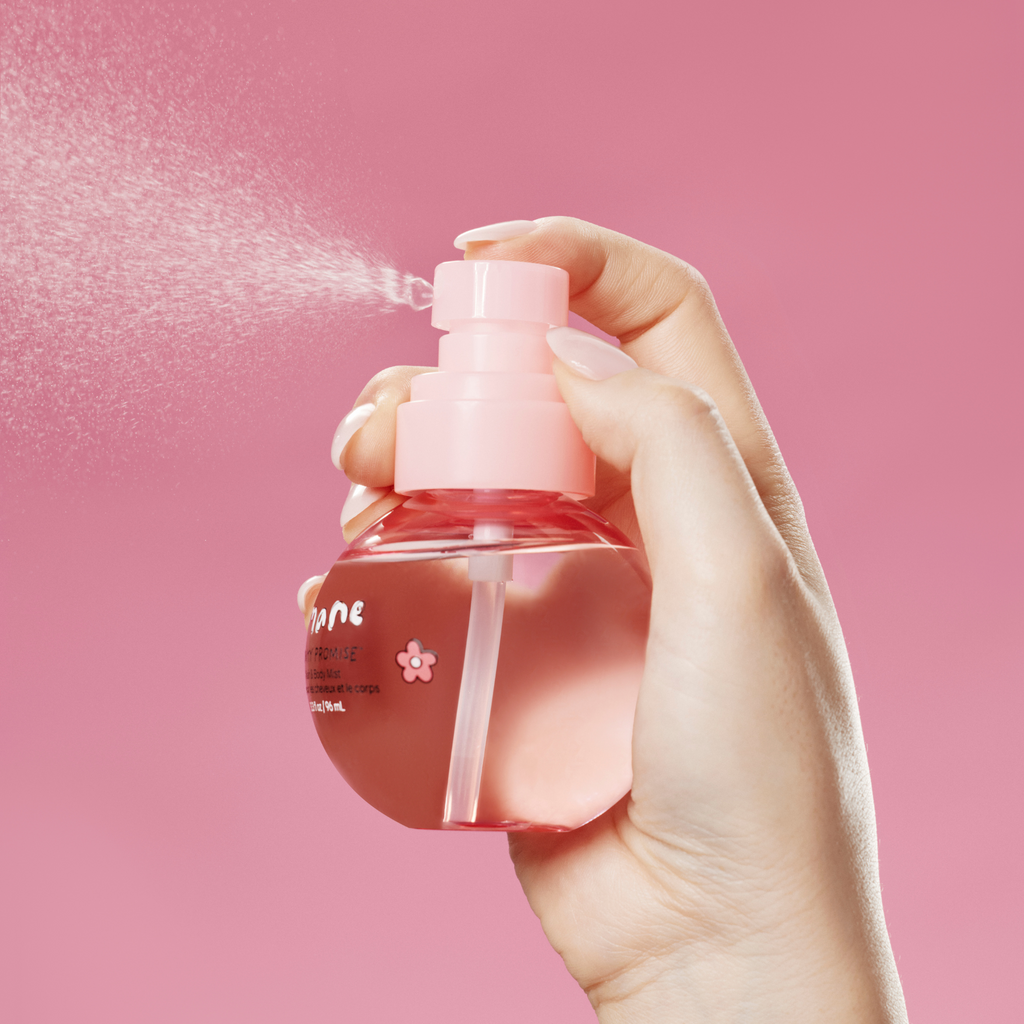 Hand holding a pink spray bottle of hair and body mist against a pink background