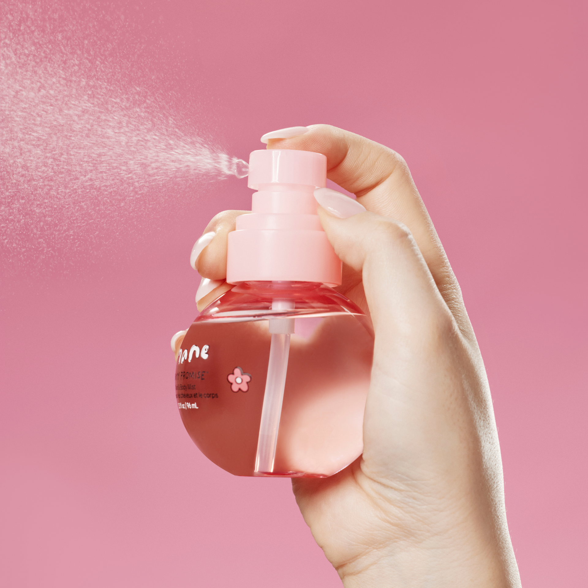 Hand holding a pink spray bottle of hair and body mist against a pink background