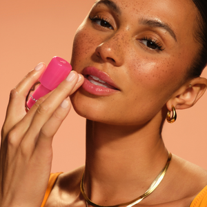Woman applying pink lipstick against a warm-toned background