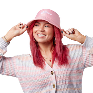 Smiling woman wearing pink bucket hat with a white logo, adjusting the brim with both hands