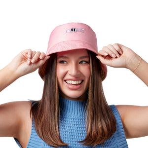 Woman wearing a pink bucket hat with a cartoon face logo, holding the brim