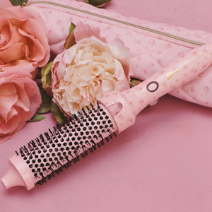 A pink hot air brush styled with pink roses on a pink background, next to its matching zippered storage case.