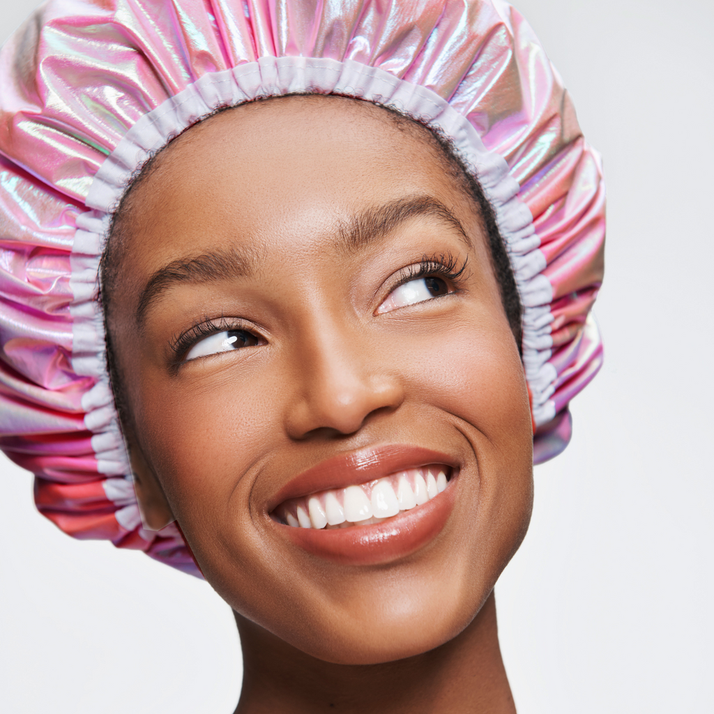 Woman wearing a shiny pink and white shower cap on a plain background