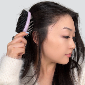 Side profile of a woman using the pink dual-sided hair brush to detangle
