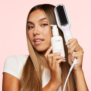 woman holding up Mane’s Hot Straightening Brush and OUAI’s Anti-Frizz Crème