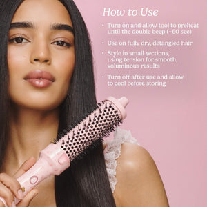 A woman with long straight black hair holds a pink hot air brush styling tool against her hair, with white text on a pink background explaining how to use the tool.