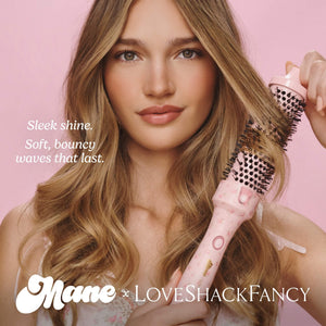 A woman with long wavy blonde hair holds a pink round brush hair styler against a solid pink background. Text on the left reads 'Sleek shine.