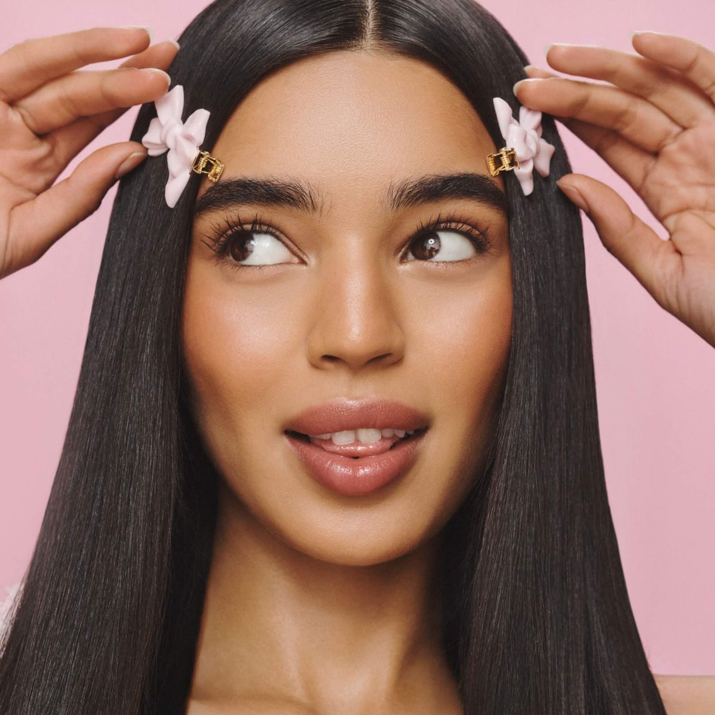 A woman with sleek dark hair placing two pink bow Creaseless Clips