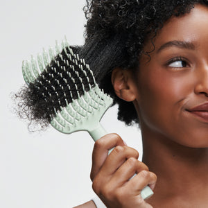 Woman brushing hair with light green brush on a white background