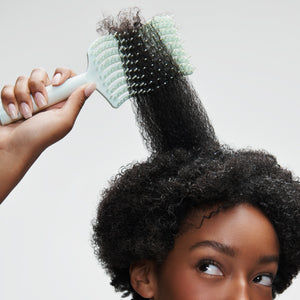Woman brushing hair up high with light green brush on a white background