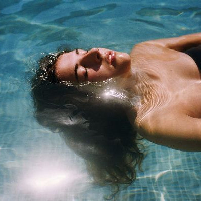Woman floating on her back in a sunlit pool with wet hair.