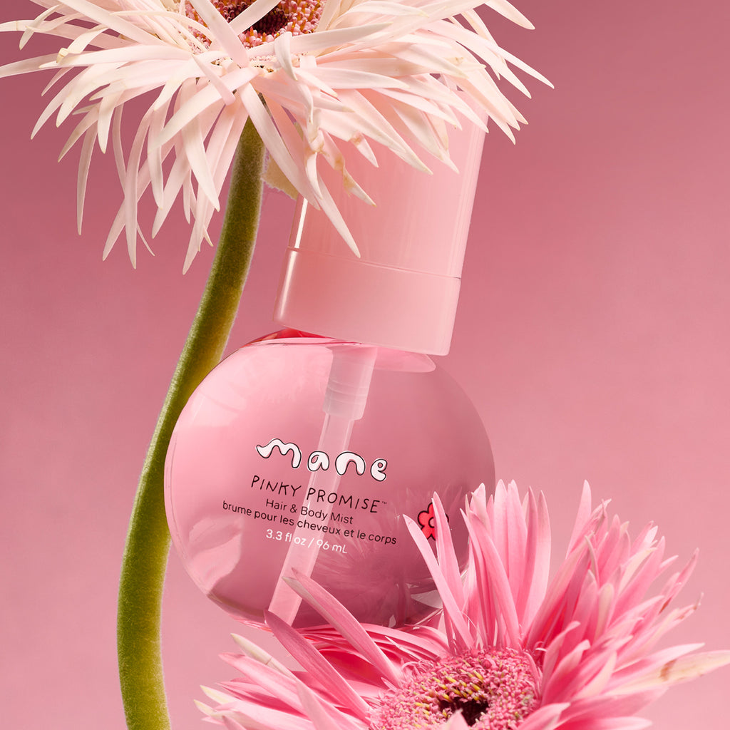 Pink bottle of 'Mane Pinky Promise' hair and body mist with pink flowers on a pink background