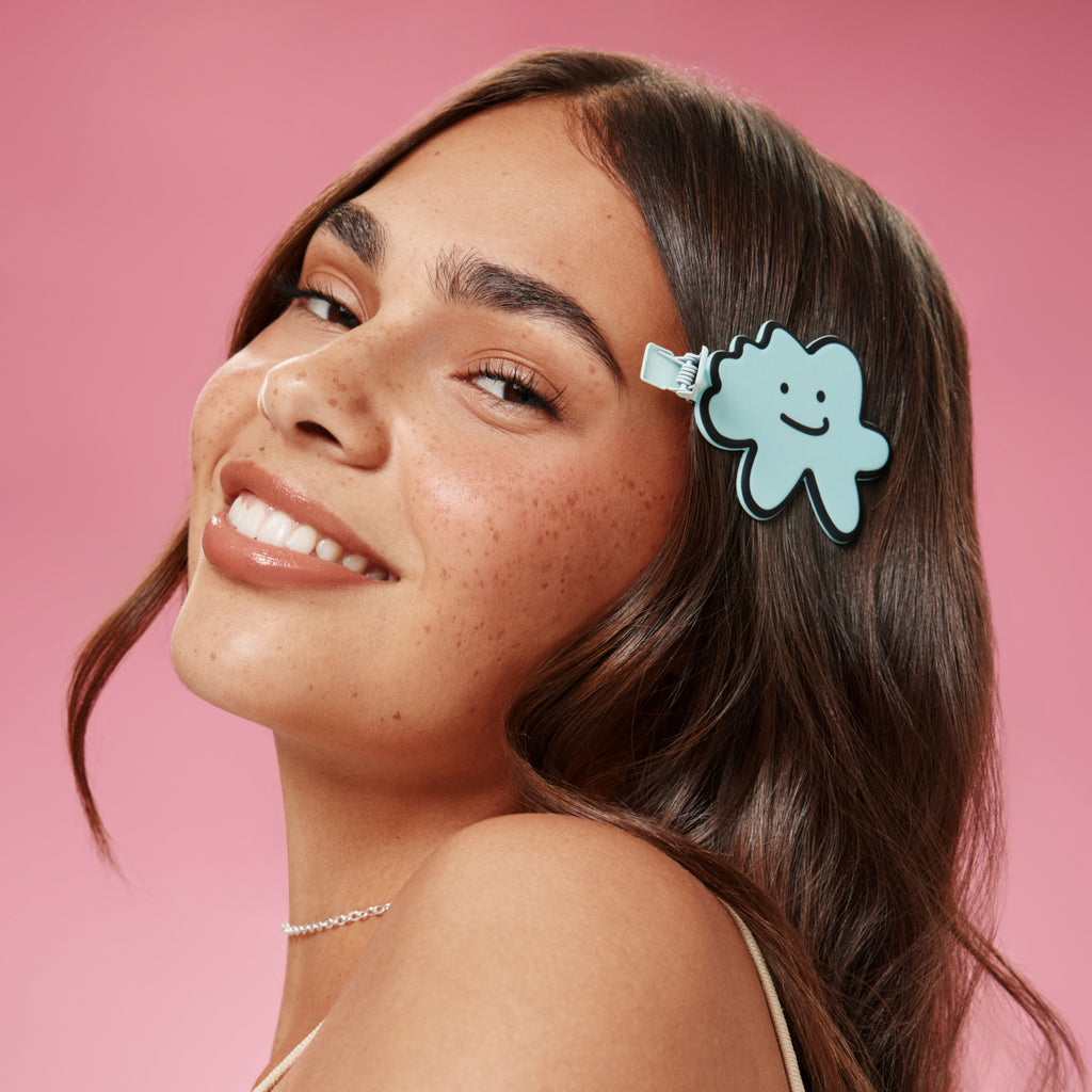 Woman with a cloud shaped hair clip featuring a smiley face design on a pink background