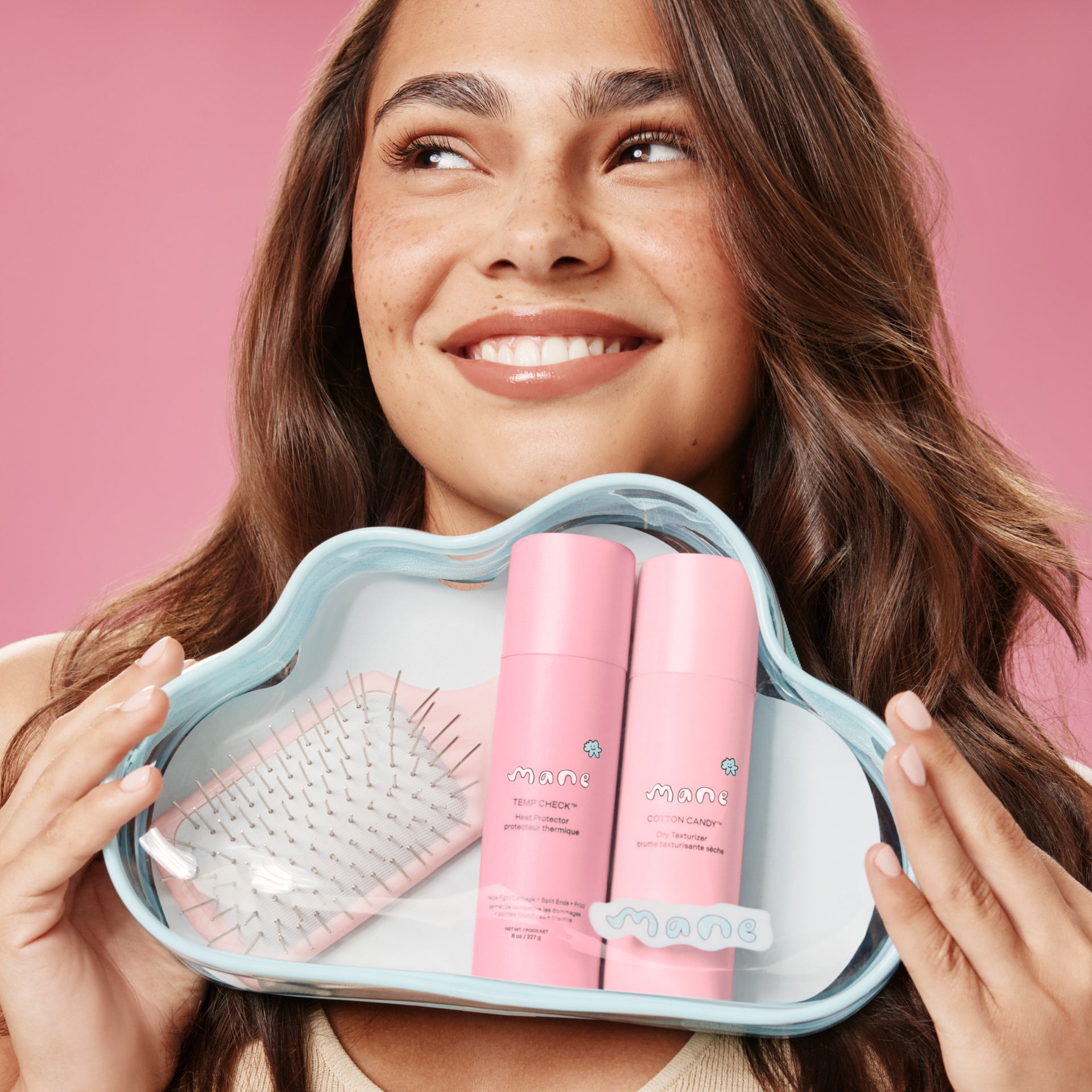 Woman holding a cloud-shaped bag with pink hair care products against a pink background