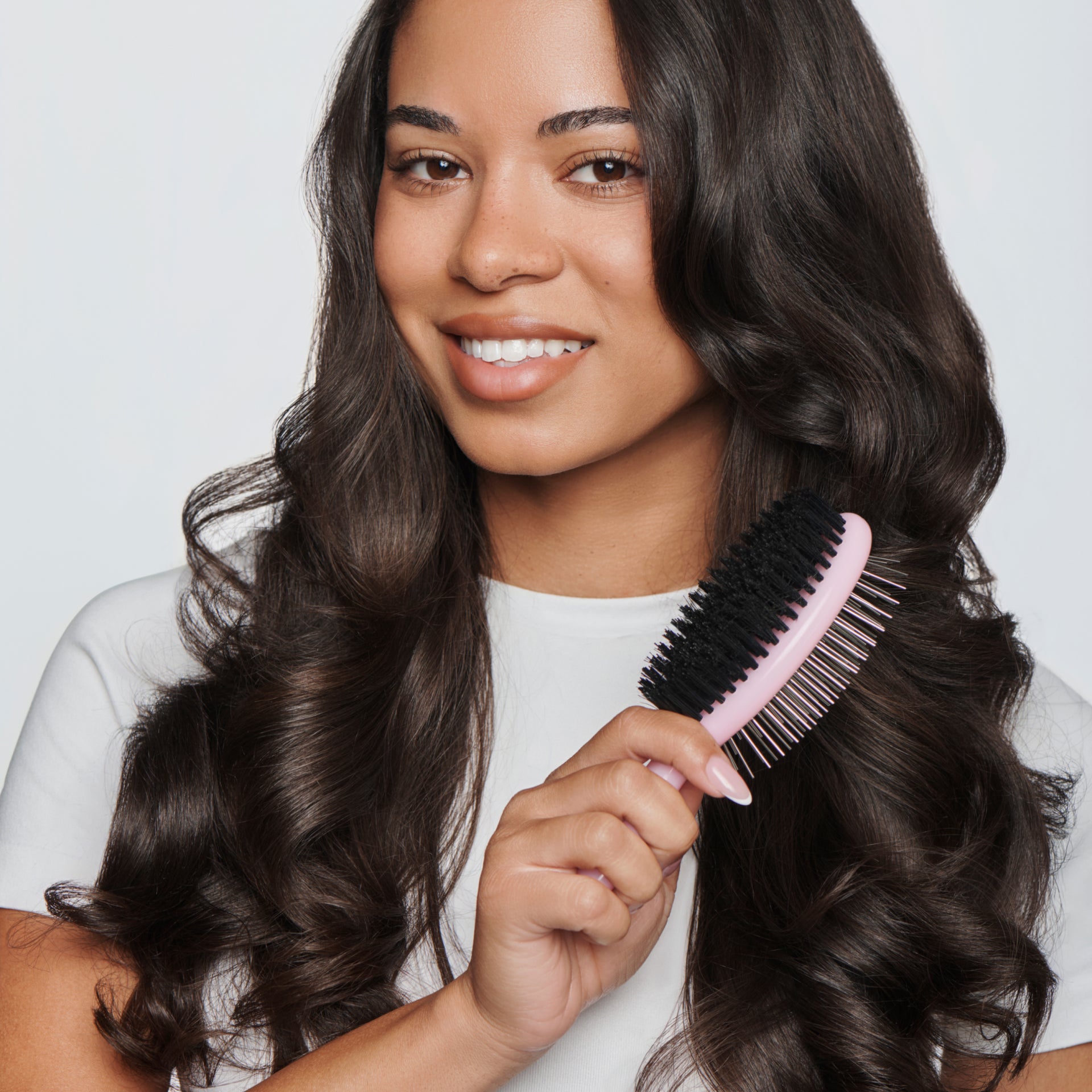 Woman with long, wavy hair holding a pink hairbrush against a plain background