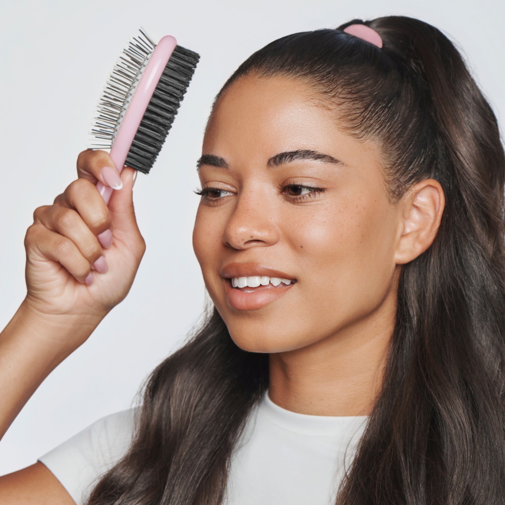Woman with a pink hairbrush and hair tied back against a plain background