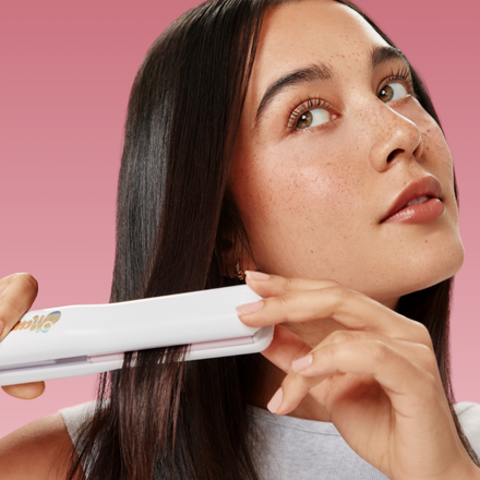 Woman using a hair straightener with a pink background