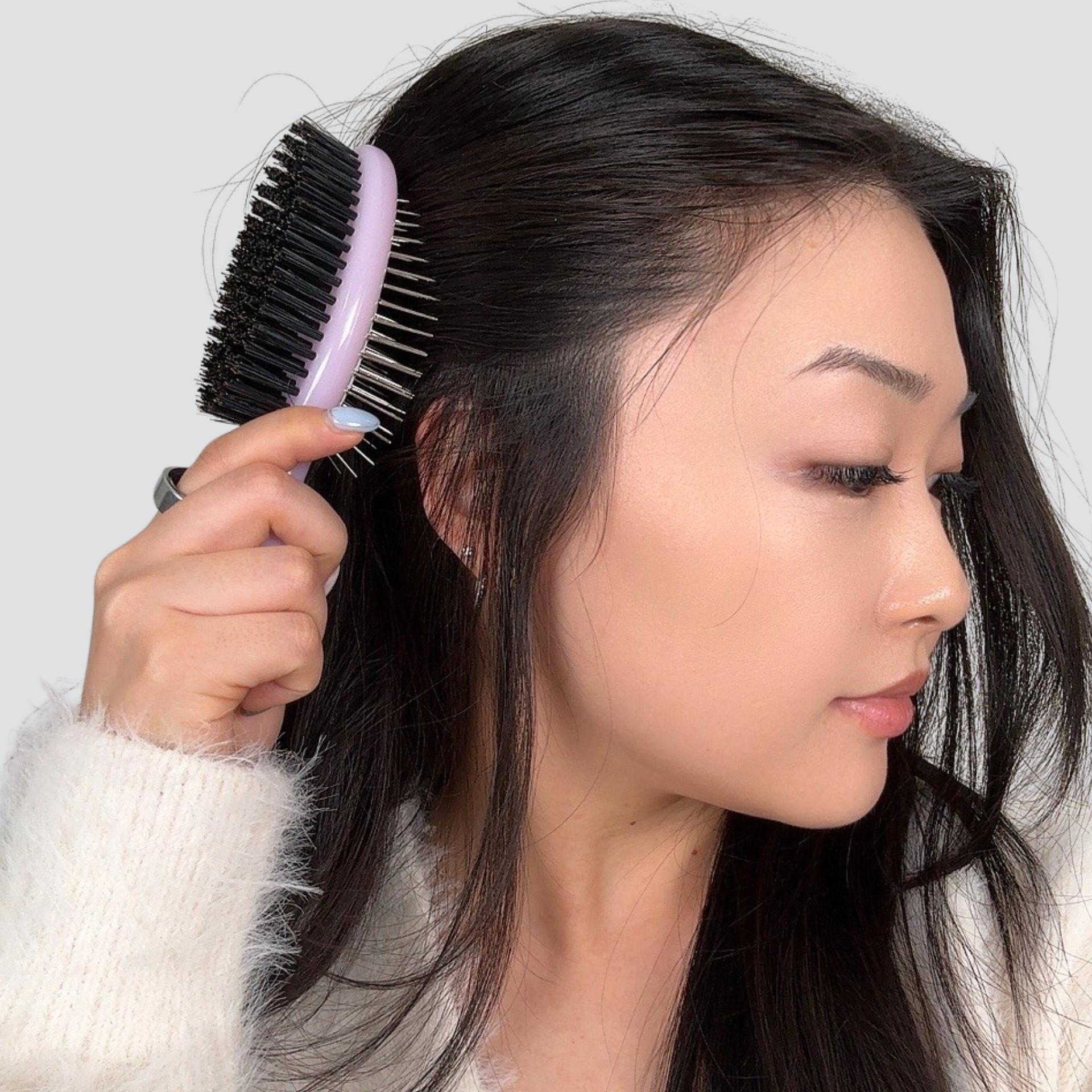 Woman brushing her hair with a purple brush against a plain background