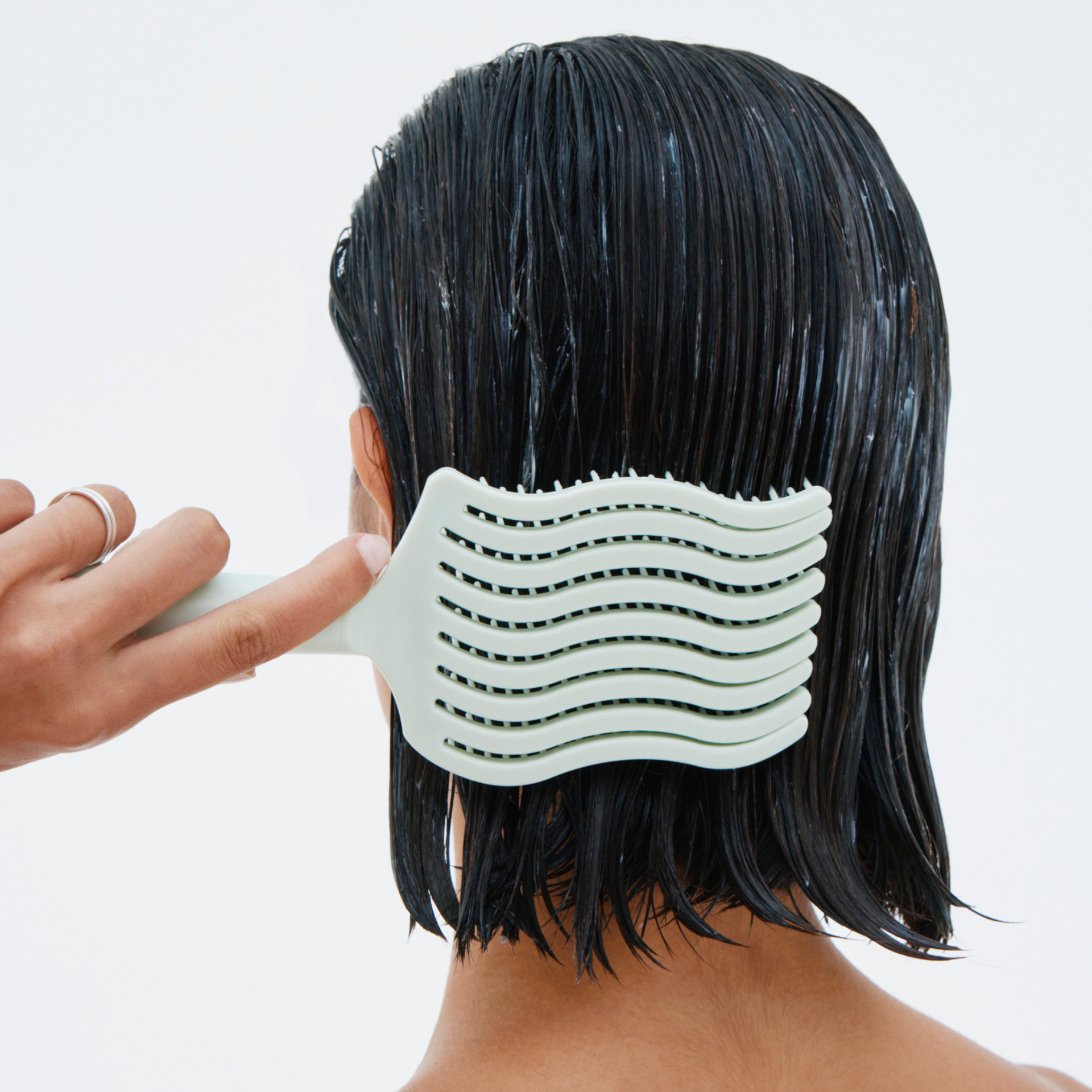 Person using a wide-tooth comb on wet hair against a white background