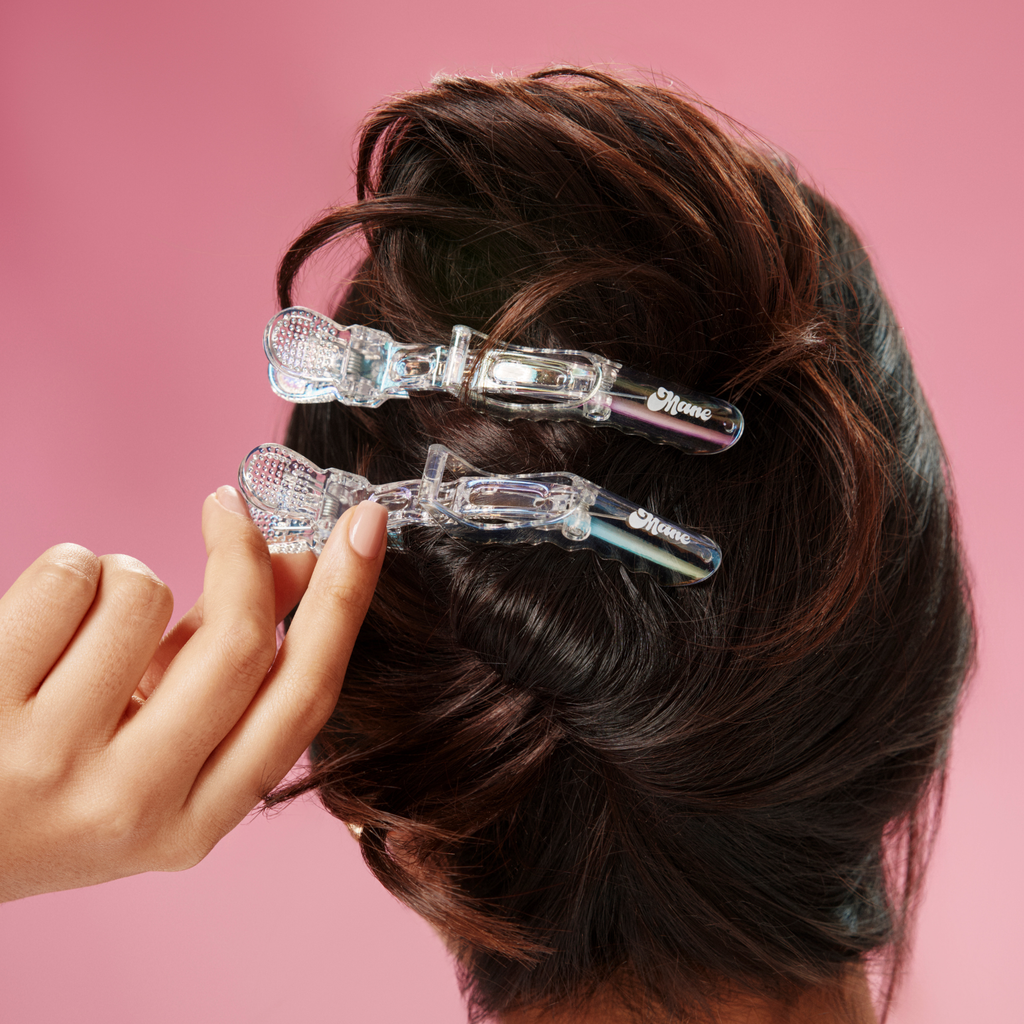 Clear hair clips being used on dark hair against a pink background