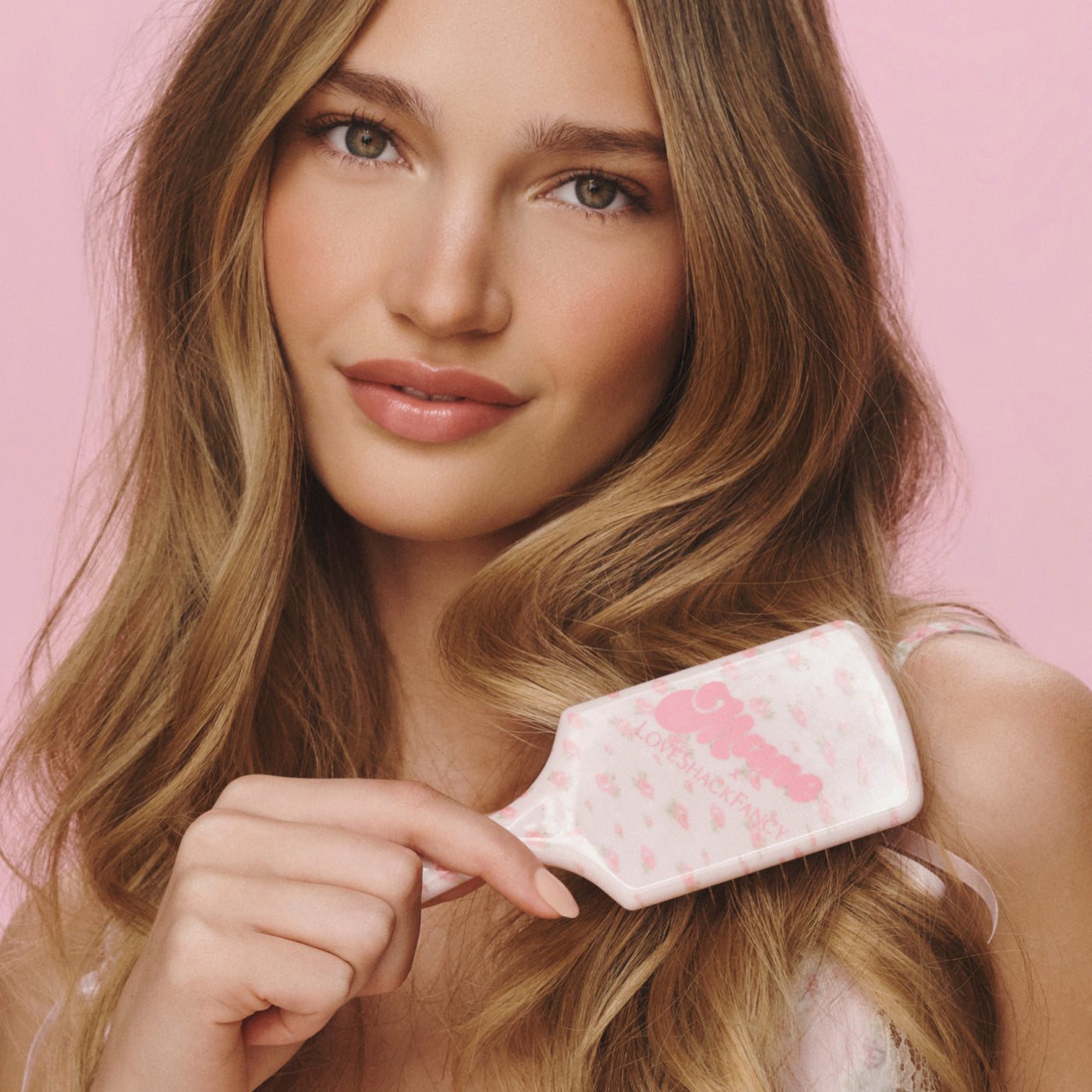 A woman with long, wavy blonde hair holding the floral Mini Detangling Brush