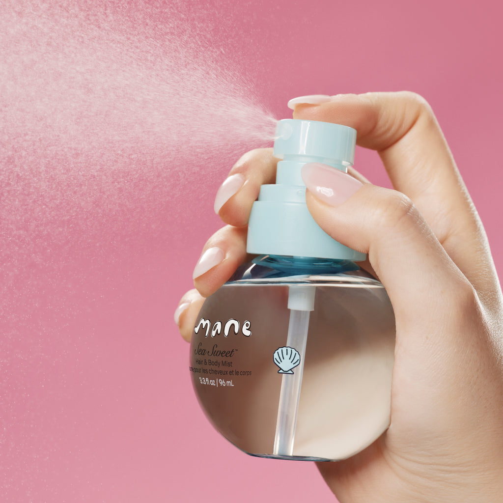 Hand holding a skincare bottle of hair and body mist labeled 'mane' against a pink background