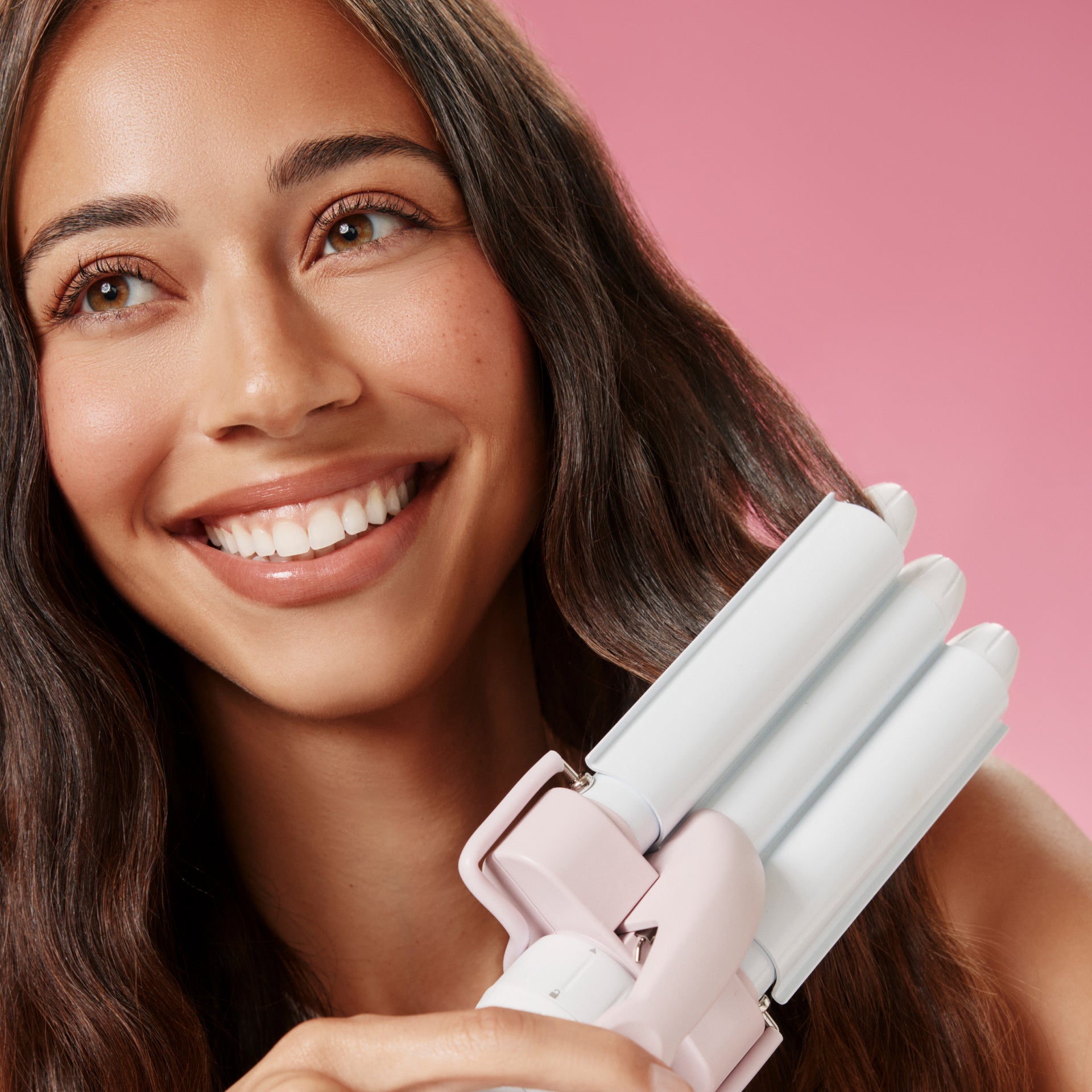 Woman holding a three barrel  hair styling tool against a pink background