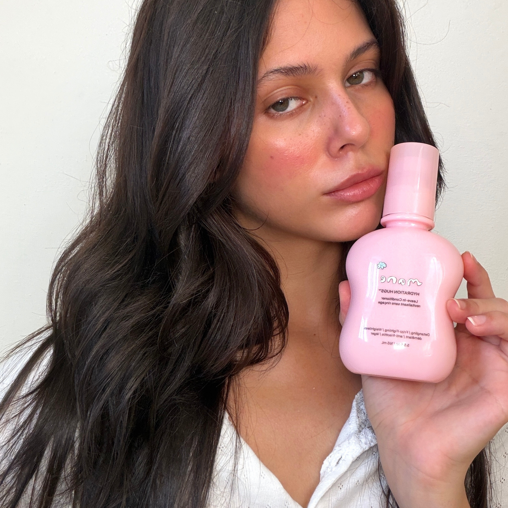 Woman holding a pink skincare bottle against a plain background